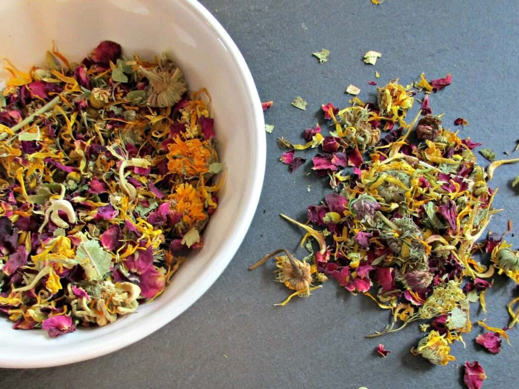 A bowl of flower petals next to some other flowers.